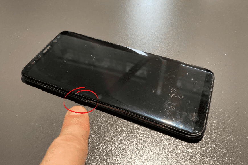 Ein Samsung Handy ist von der Seite zu sehen, wobei der mit dem Zeigefinger auf dem Bixby Button gezeigt wird